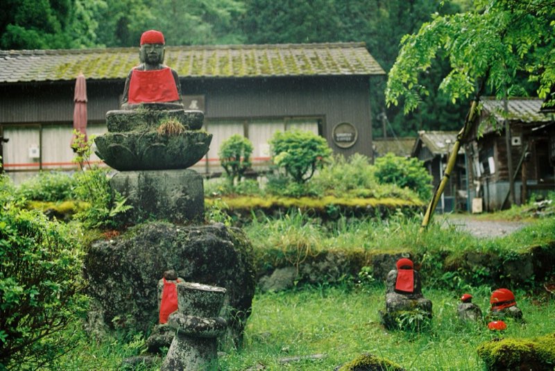 Stone figures in red bibs standing in wet grass in the rain.